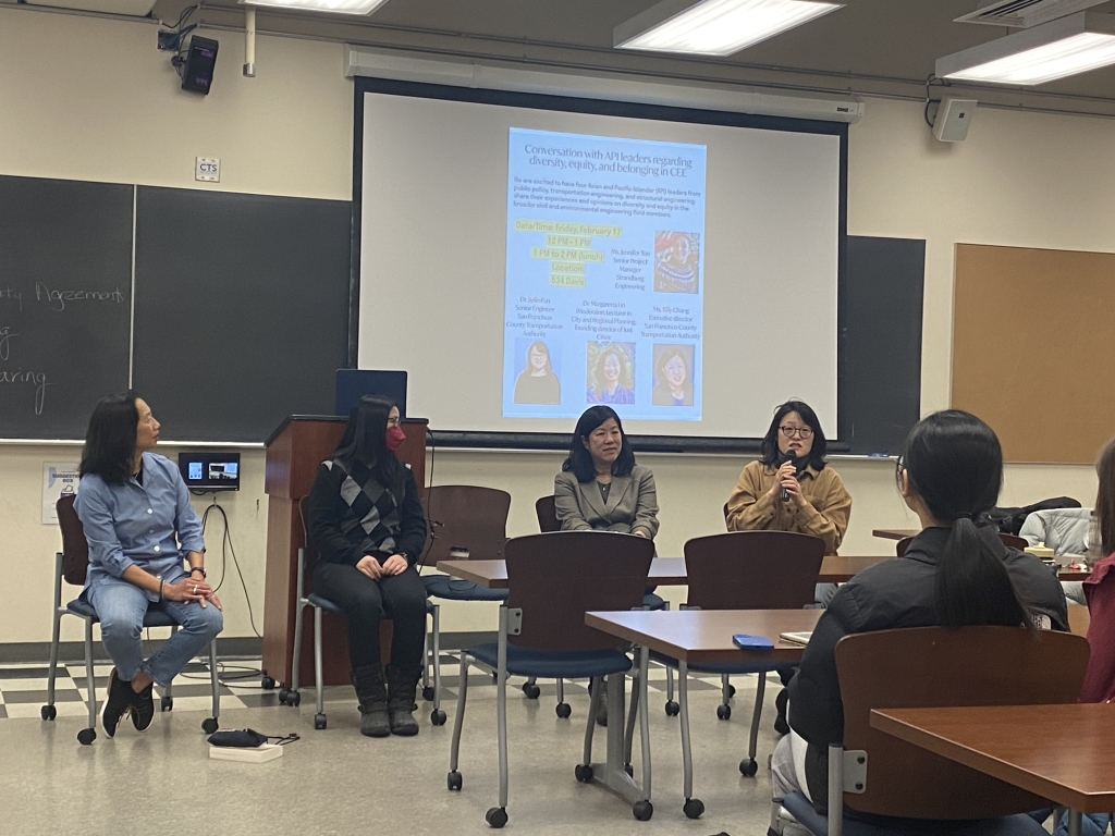 Seated students and standing professor look at screen located in foreground of photo.