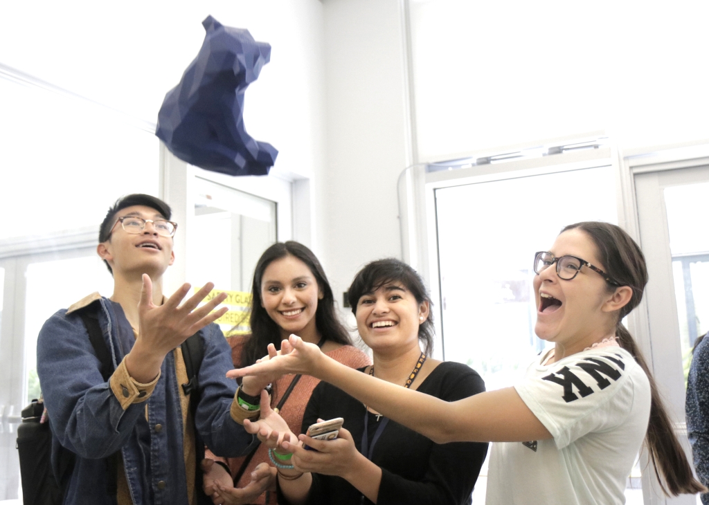 Group of students tossing bear figurine in the air.