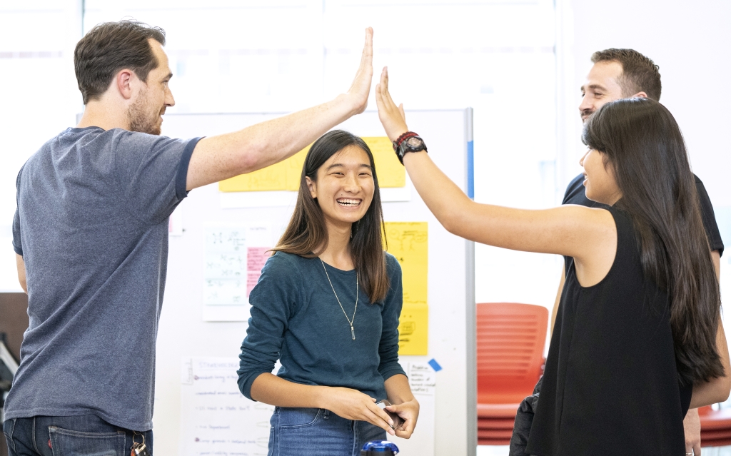 Two high-fiving individuals frame a third person below their hands.