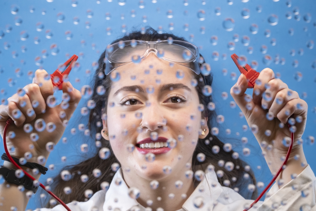 Woman holding cable with two hands, up to a clear glass panel with water droplets.