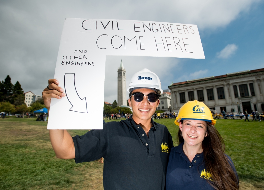 Two students with hardhats, holding sign that says "civil engineers come here."