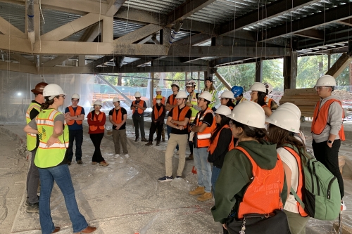 A group of students wearing protective gear stands at the construction site of the Undergraduate Academic Building