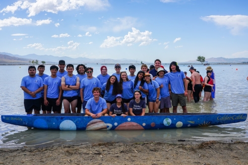 A group photo of the Cal Concrete Canoe team standing in front of their concrete canoe design in the water at the ASCE Concrete Canoe Competition. (Photo Credit: Brenda Ruby Aguilar)